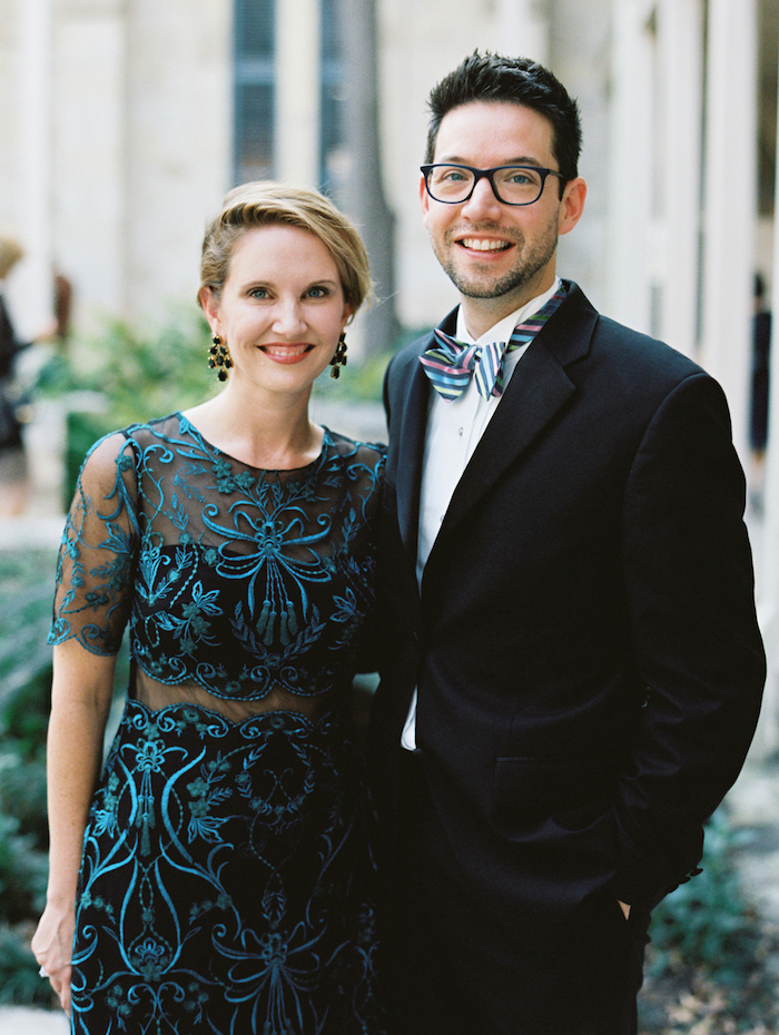 man and woman wearing black suit with colorful bow tie and black dress with blue lace on top and short sleeves what to wear to a winter wedding