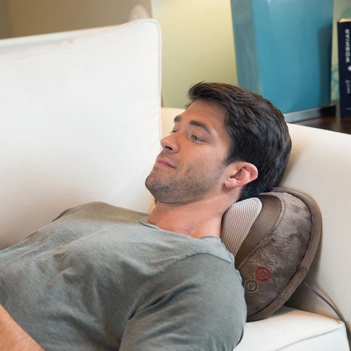 man wearing gray shirt laying on white sofa unique gifts for dad shiatsu massager pillow under his neck