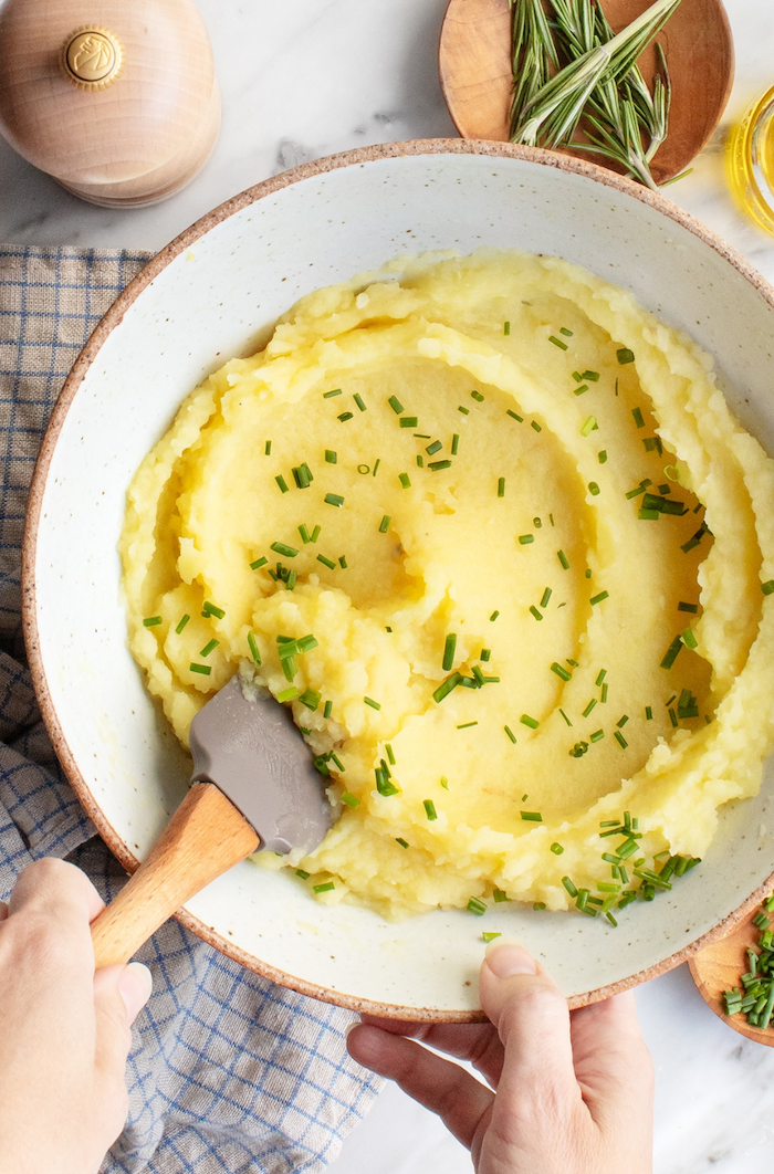 mashed potatoes in white ceramic bowl garnished with wild onion best thanksgiving side dishes stirred with gray spatula