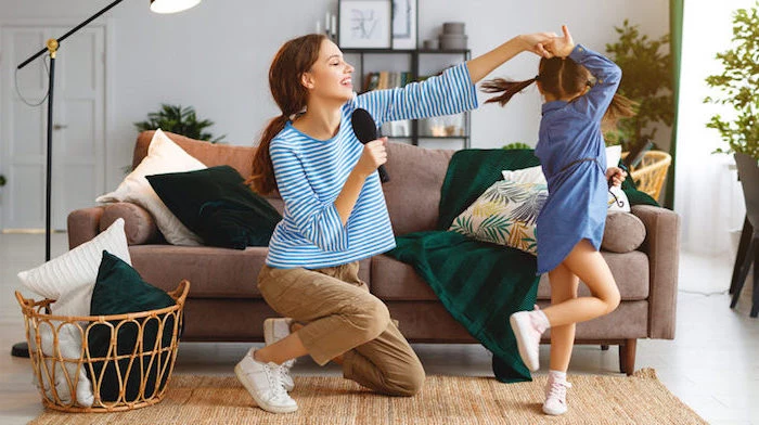 mom and daughter singing and dancing in front of brown sofa activities for kids at home white and green throw pillows and blanket