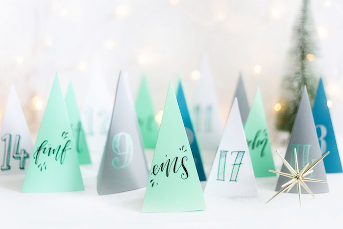 paper in the shape of christmas tree in different colors white gray blue mint green placed on white surface advent calendar