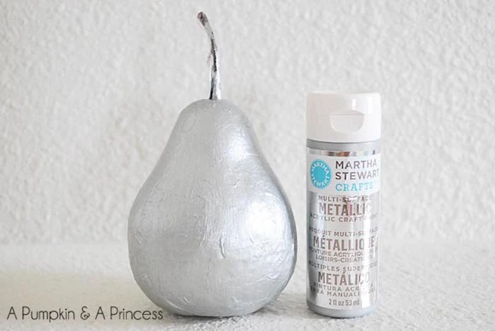 pear shaped ornament painted silver bottle of silver paint next to it christmas tree decorations 2020 placed on white surface