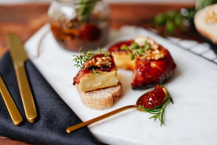 piece of baked brie wrapped in prosciutto on slice of bread thanksgiving food ideas covered with jam thyme walnuts