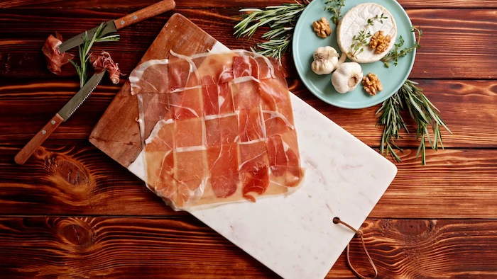 prosciutto slices arranged together thanksgiving dinner ideas spread on marble cutting board placed on top of wooden surface