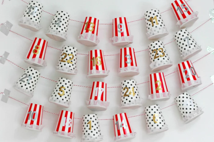 red white and black paper cups labeled with numbers hanging from red and white strings hanging on white wall homemade advent calendar