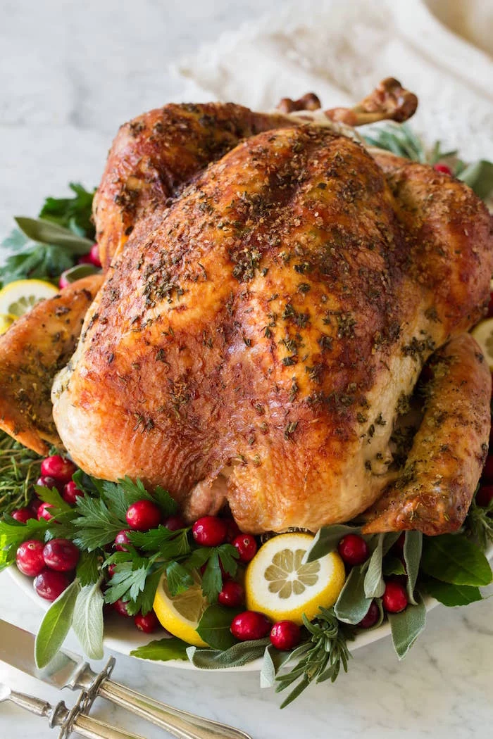 roasted christmas turkey placed on white tray easy christmas dinner ideas decorated with green herbs cranberries lemon slices