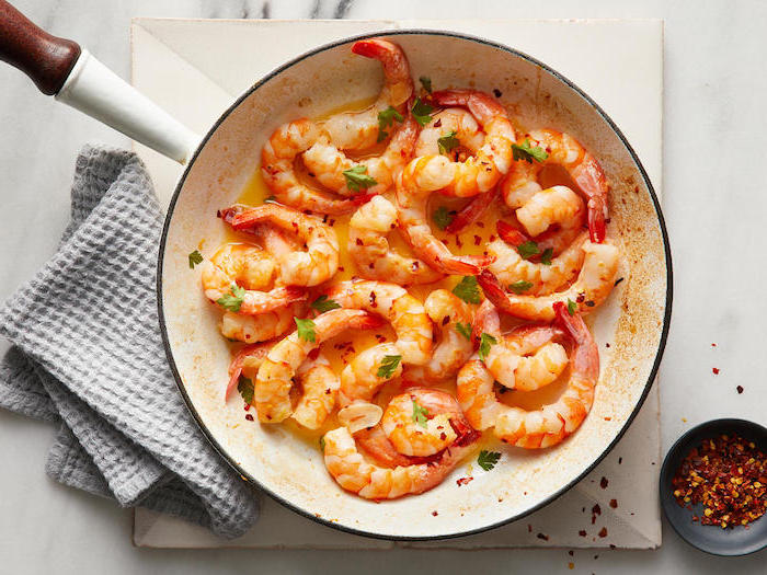 sauteed shrimp in white sauce pan garnished with chopped porsley garlic butter shrimp red pepper flakes in black bowl on the side