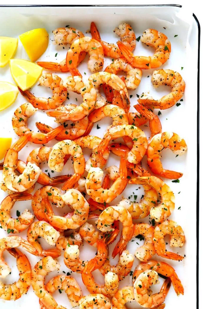 shrimp dinner ideas shrimp with herbs arranged on paper lined white baking sheet lemon wedges on the side