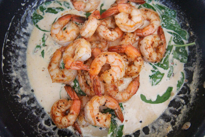 shrimp placed in creamy garlic butter sauce with spinach inside black saucepan how long to cook shrimp