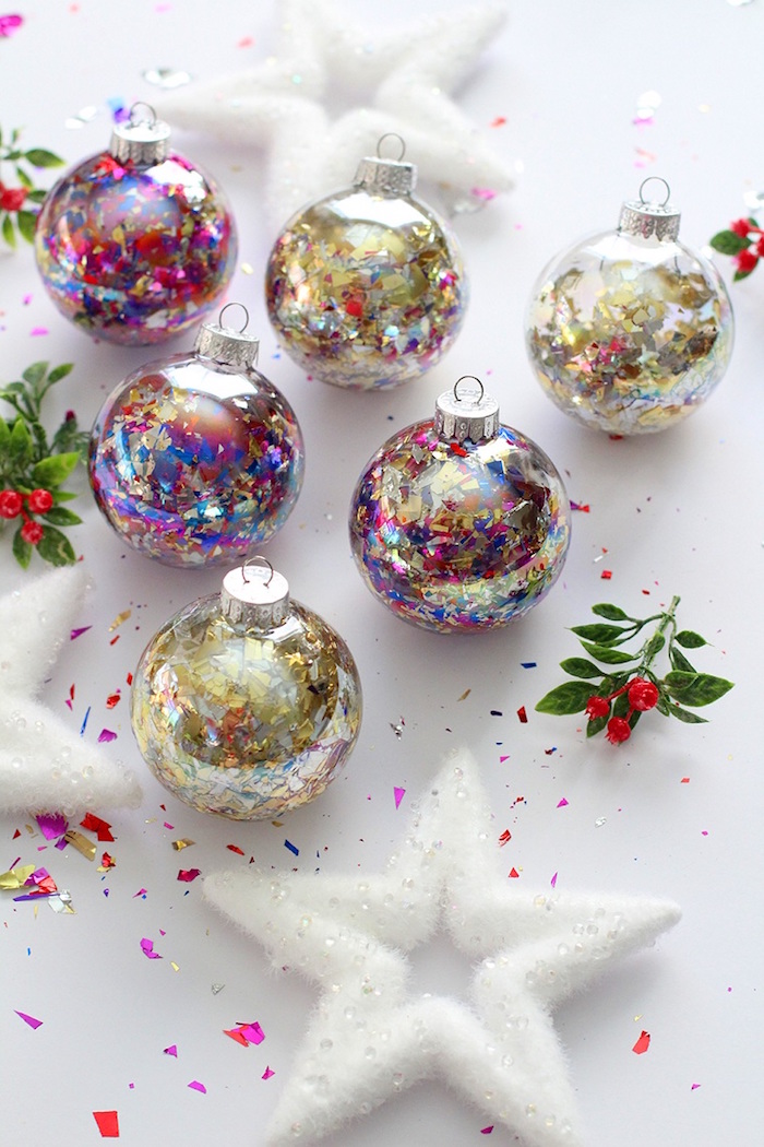 six ornaments filled with glitter and colorful confetti christmas tree decorations 2020 placed on white surface with white star shaped ornaments