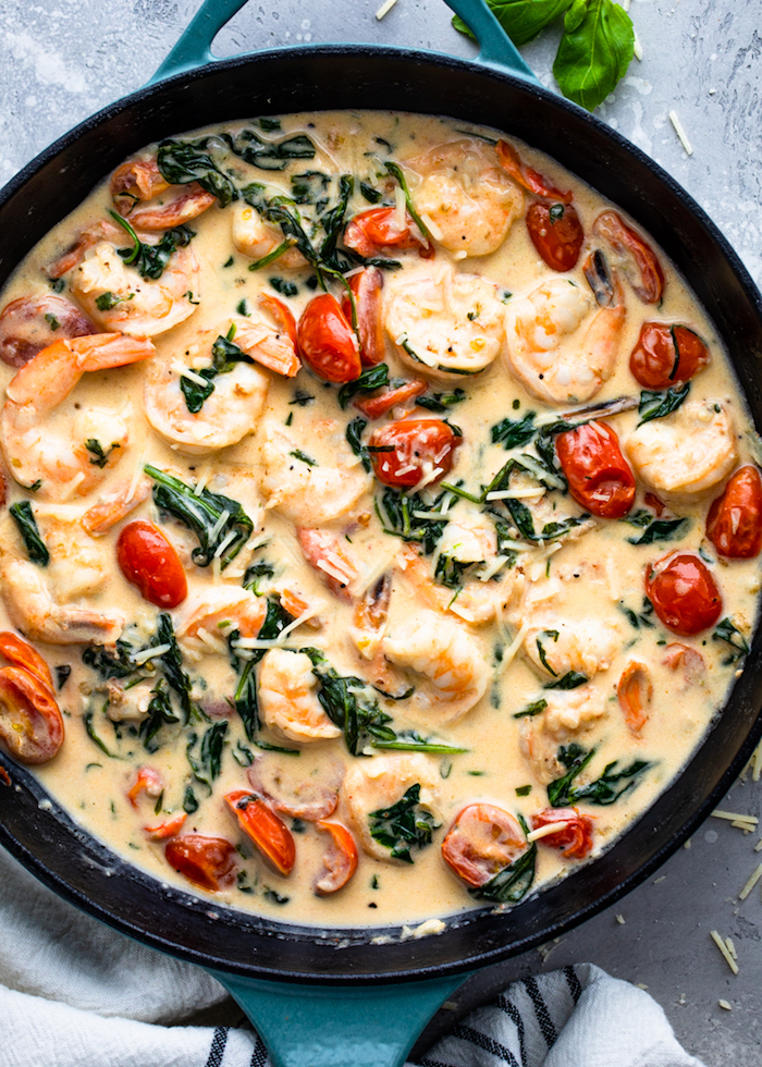skillet filled with creamy tuscan shrimp baked shrimp recipes with spinach cherry tomatoes and grated parmesan cheese