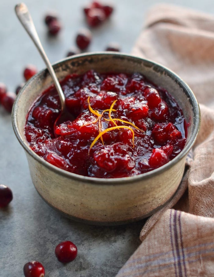 small ceramic bowl filled with cranberry sauce garnished with lemon zest christmas ham dinner spoon on the side