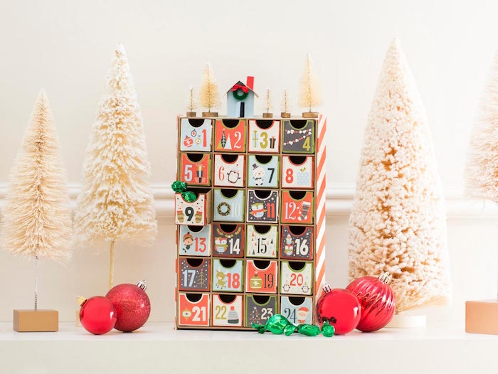 small wood christmas countdown calendar with little boxes with numbers decorated in different colors small white faux trees around them red baubles