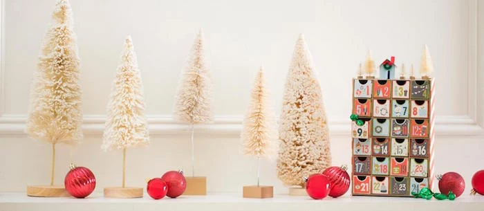 small wood christmas countdown calendar with little boxes with numbers decorated in different colors small white faux trees around them