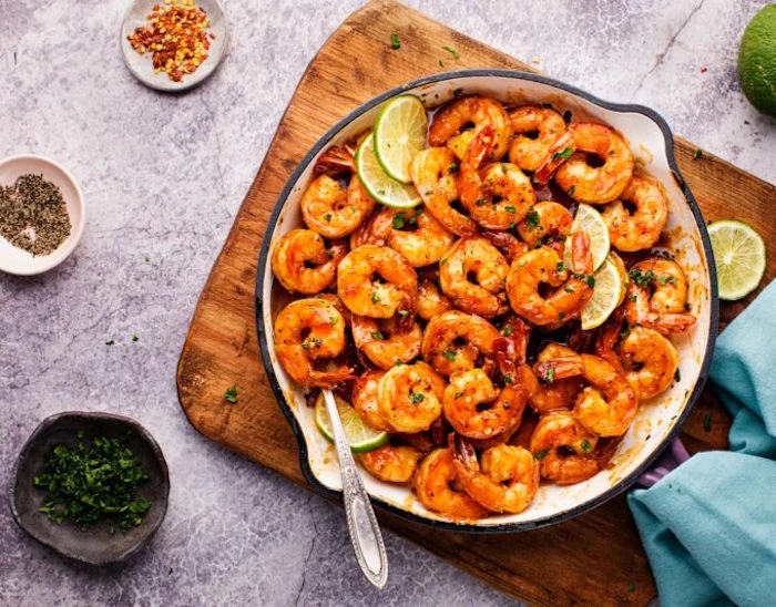 spicy honey lime shrimp baked in white skillet how long to cook shrimp placed on wooden cutting board bowls with herbs on the side