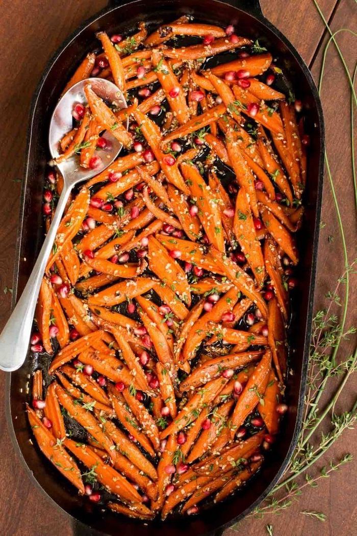 spoon inside black baking dish easy thanksgiving side dishes honey roasted carrots with pomegranate seeds