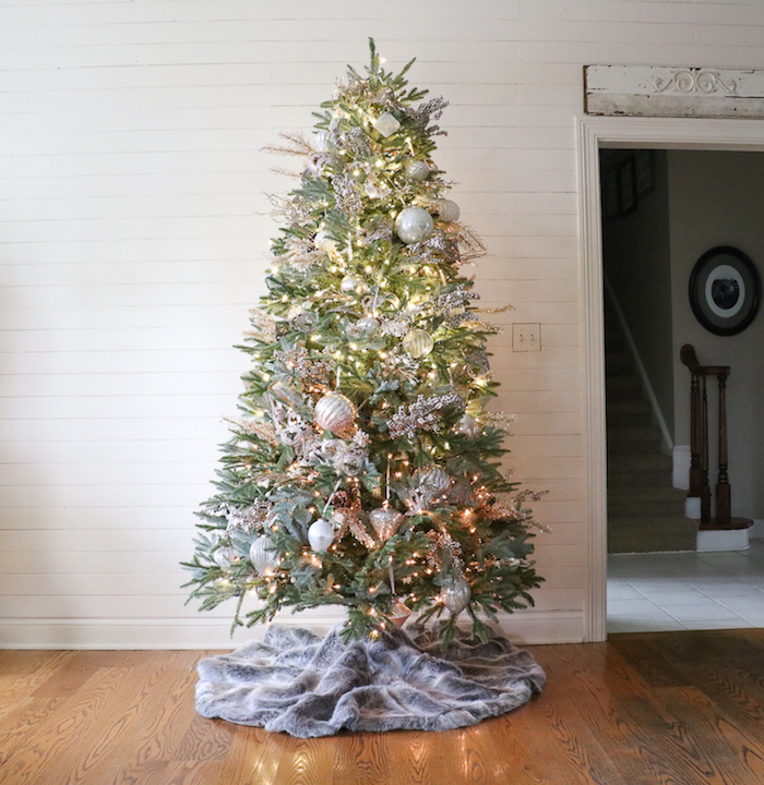 tall tree with lots of lights silver gold baubles and ornaments gray skirt placed on wooden floor how to decorate a christmas tree with ribbon