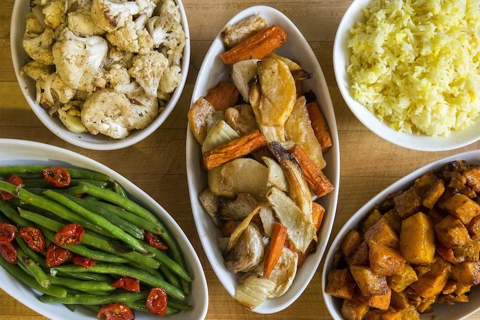 thanksgiving side dishes wooden surface five white plates on it with different dishes beans rice cauliflower potatoes carrots