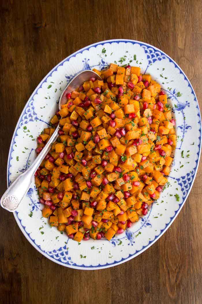 thanksgiving vegetable side dishes roasted carrots with pomegranate seeds in blue and white plate spoon on the side