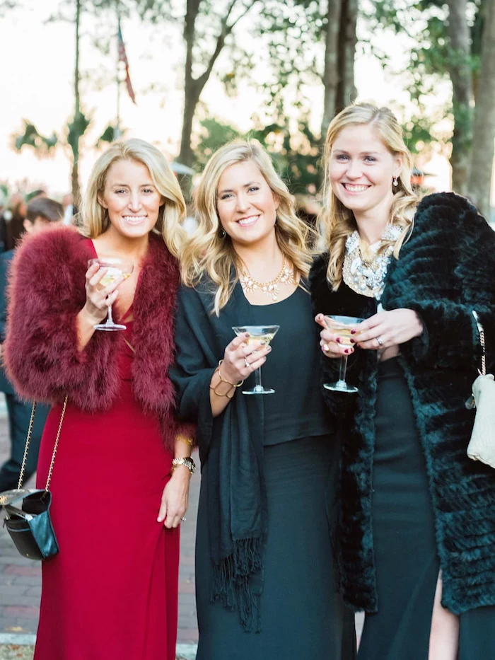 three women wearing olive green and red dresses formal dresses for weddings wearing furry coats in green and red