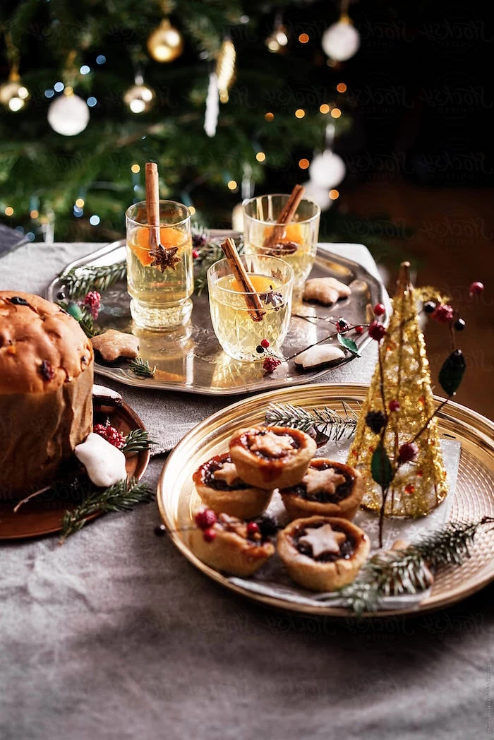 two metallic trays one with three glasses with cocktails another with small cupcakes christmas eve dinner ideas christmas tree in the background