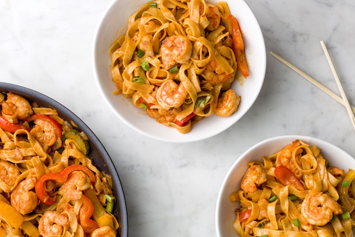 two white plates filled with noodles with shrimp and peppers how to cook shrimp saucepan on the side placed on marble countertop