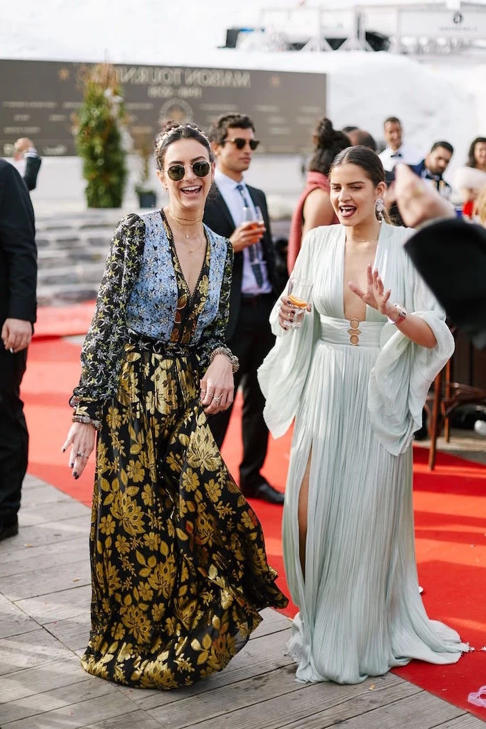 two women walking on red carpet winter wedding guest dresses both wearing dresses with long sleeves deep necklines