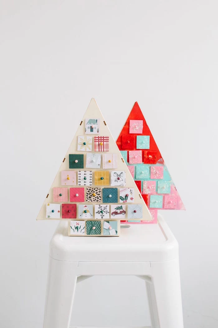 two wood christmas trees placed on white side table advent calendar little boxes attached to them decorated in different colors