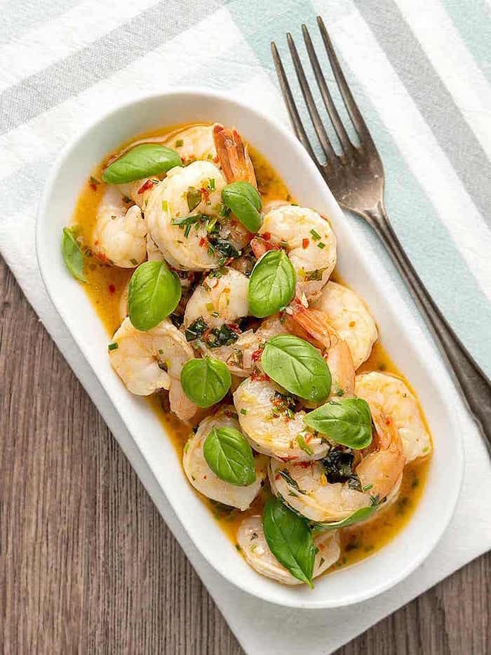 white plate filled wiith cooked shrimp with sauce how to cook shrimp garnished with fresh basil leaves fork on the side