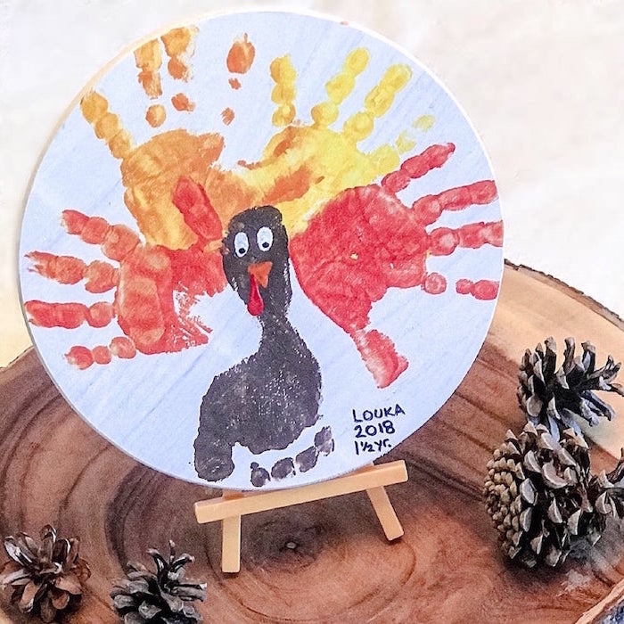 white wooden round board turkey drawn on it with handprints indoor activities for kids placed on wooden log slice with pinecones