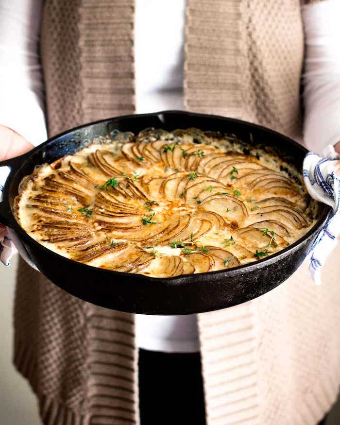 woman holding black skillet best thanksgiving side dishes creamy potatoes au gratin inside