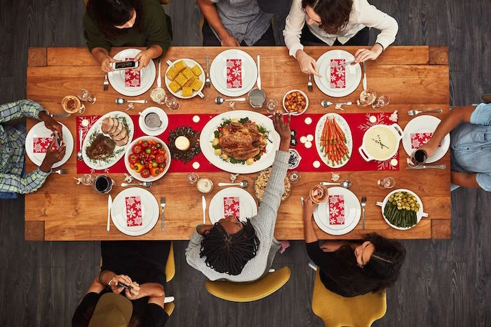 wooden table with red table runner christmas eve dinner ideas eight people sitting around it white plates and different dishes