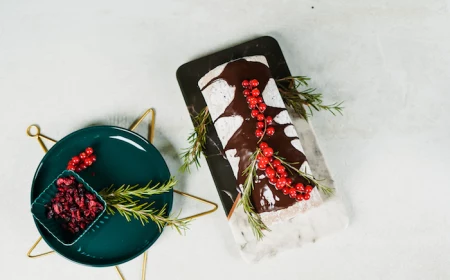 yule log christmas dessert placed on black and white marble board easy christmas dinner ideas decorated with rosemary and cranberries