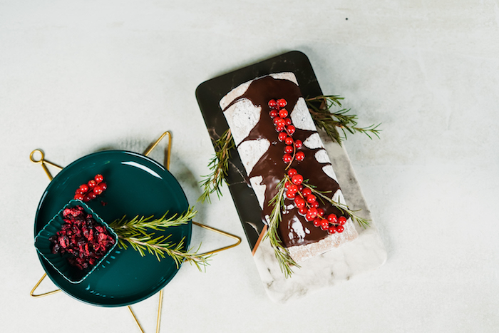 yule log christmas dessert placed on black and white marble board easy christmas dinner ideas decorated with rosemary and cranberries