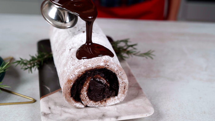 yule log dessert rolled up christmas party food ideas buffet melted chocolate being poured on it from small metal jug