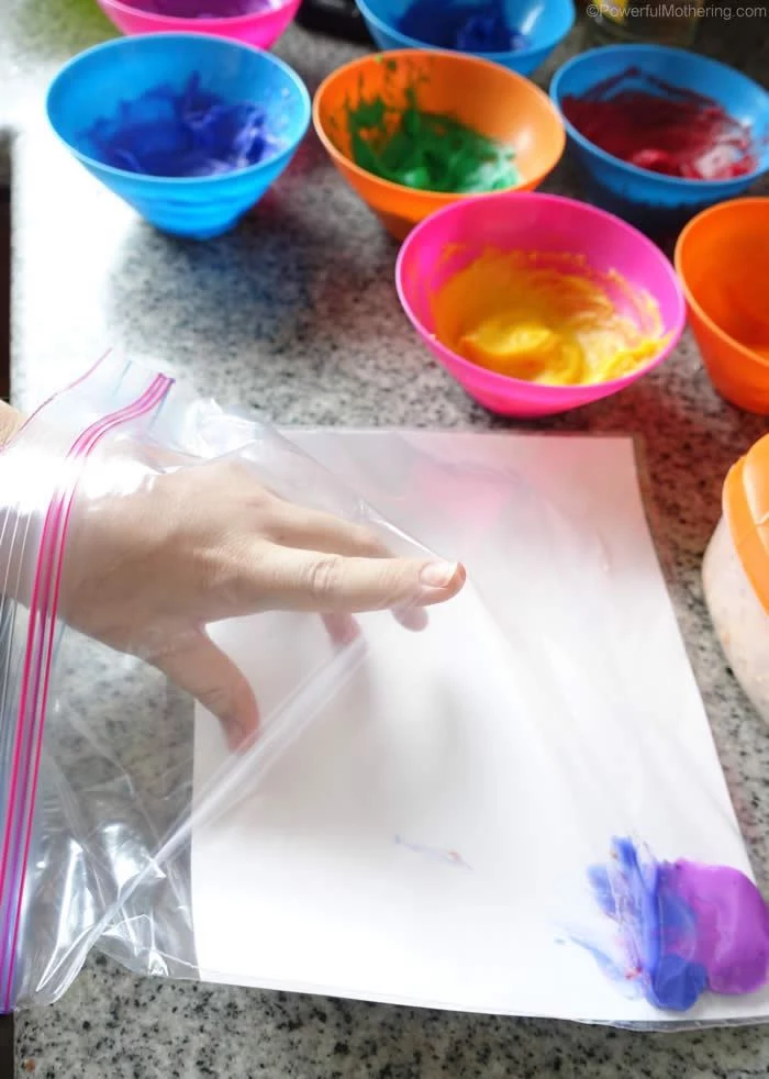 ziploc bag with purple and blue paint inside things to do with kids at home lots of bowls next to it with paint in different colors