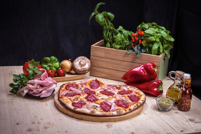basil in wooden crate placed on wooden table homemade pizza dough salami pizza with mushrooms placed on wooden cutting board