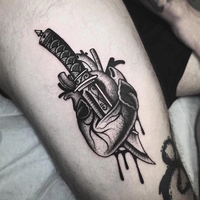black anatomically correct hear with dagger going through it blood dripping heart tattoo on wrist thigh tattoo