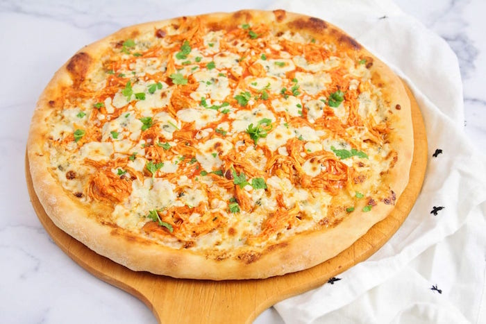 buffalo chicken pizza easy pizza dough recipe with cheese garnished with chopped parsley placed on wooden cutting board