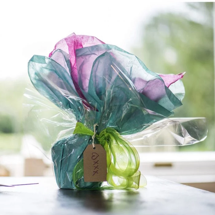 ceramic mug being wrapped in pink and turquoise tissue paper diagonal gift wrapping tied with green tulle ribbon