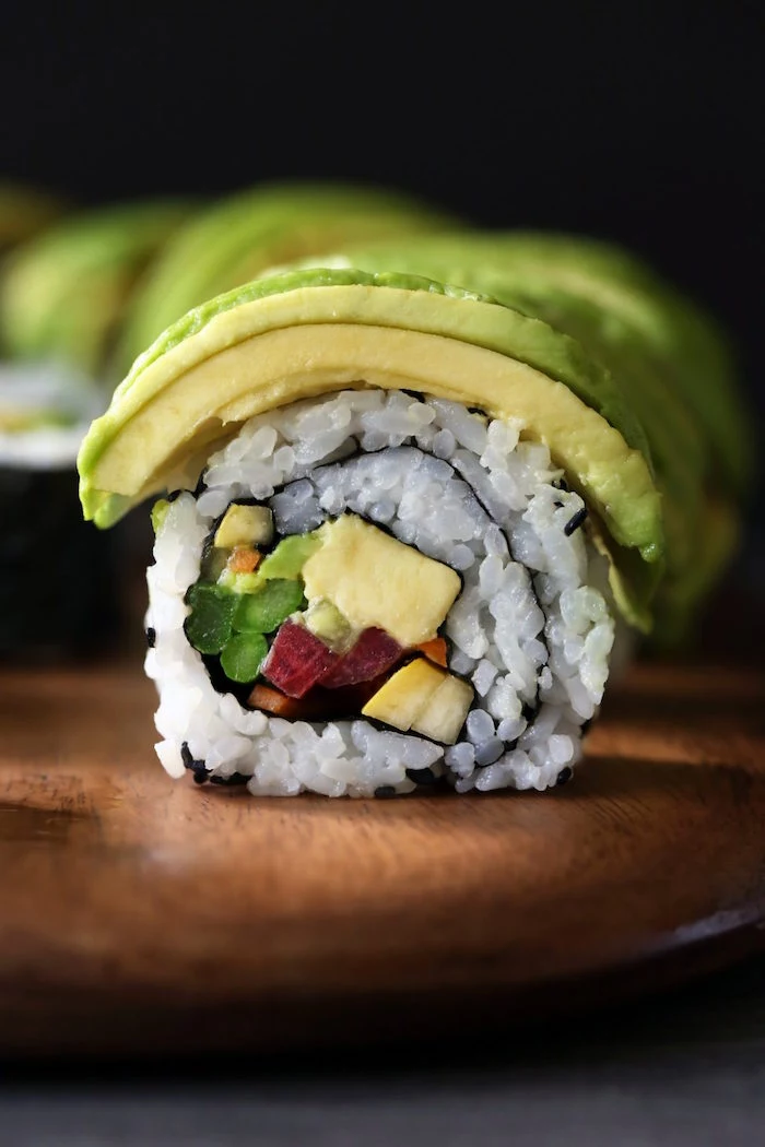 close up photo of vegetable sushi rolls with rice avocado cucumbers how to make sushi at home placed on wooden cutting board