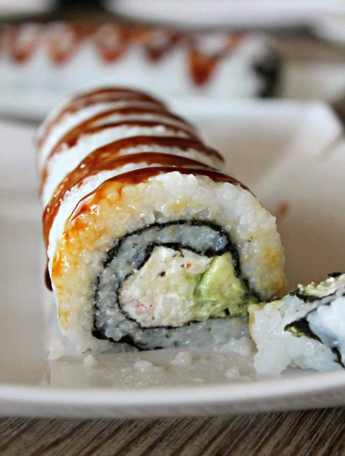 crab roll with avocado rice dragon roll sushi placed on white plate drizzled with soy sauce