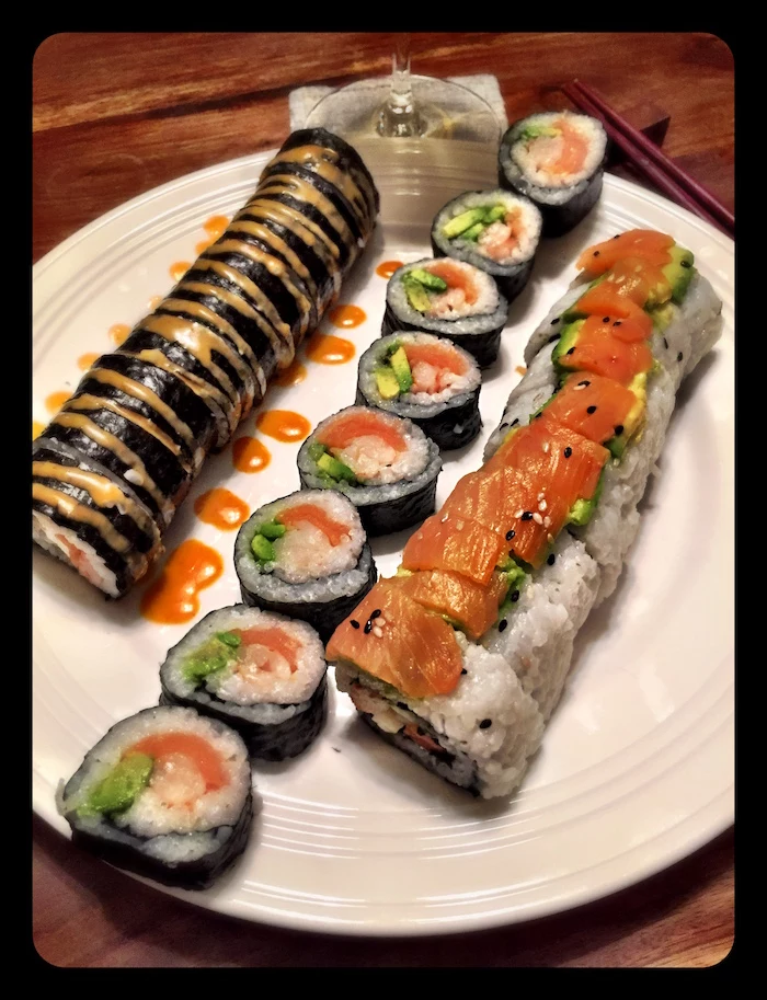 different types of sushi with salmon arranged on white plate shrimp tempura roll drizzled with different types of sauce