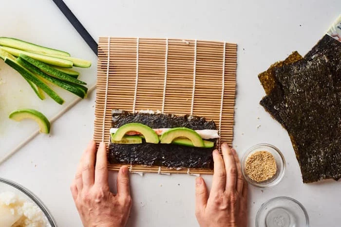 dragon roll sushi nori sheet avocado rice spread out on bamboo rolling mat placed on white surface