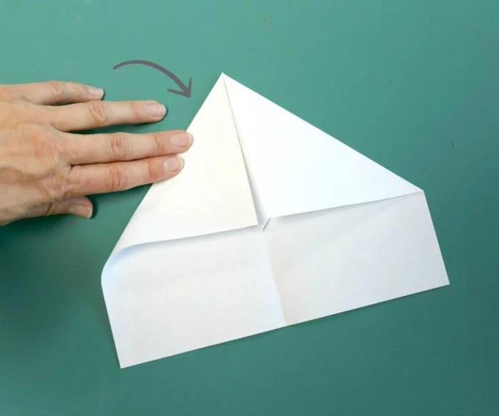folding a piece of white paper on turquoise background paper airplane instructions diy tutorial step by step