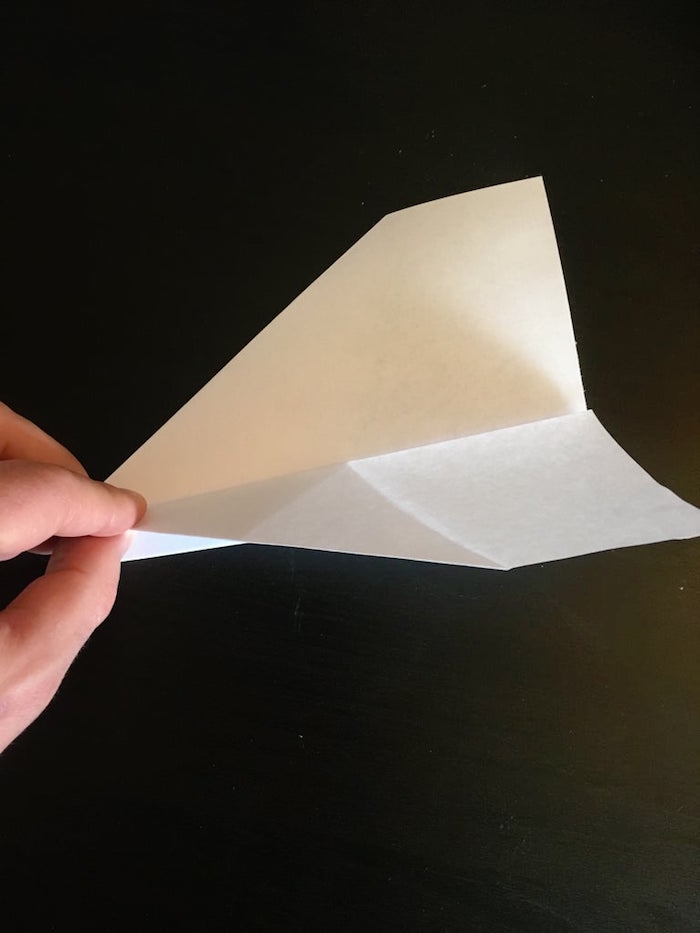 hand holding a white piece of paper best paper airplane design being folded into a plane