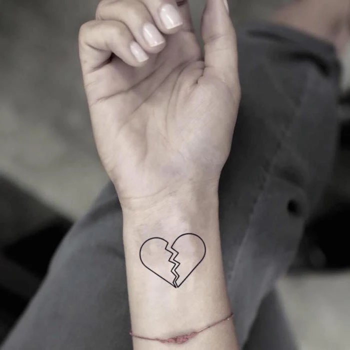 heart tattoo on hand black outlines of heart broken in the middle wrist tattoo on woman wearing red thread as bracelet