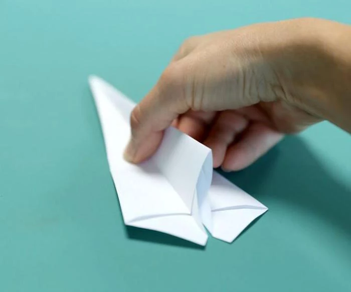 how to make a paper airplane easy folding a piece of white paper into a plane on turquoise background