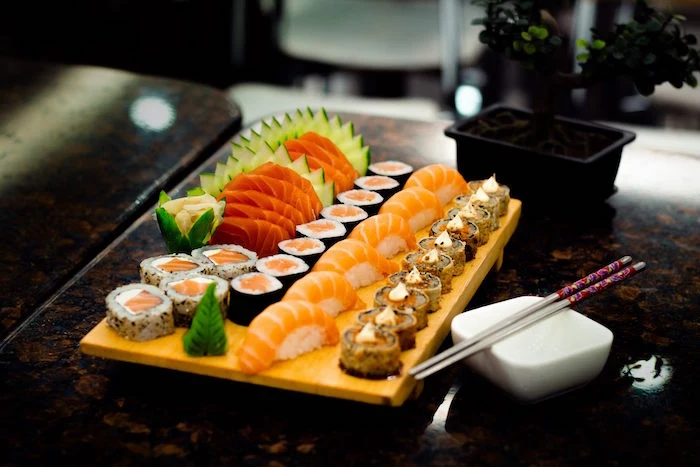 how to make sushi rice wooden platter covered with different types of sushi with salmon cucumbers placed on dark surface