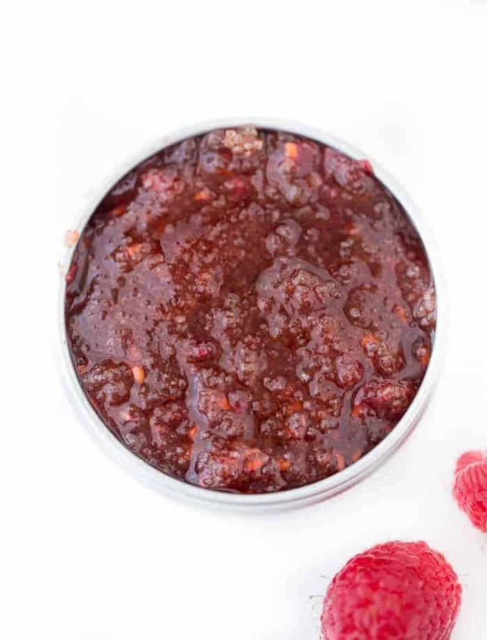 lip scrub made with raspberries poured into small plastic container how to make a sugar lip scrub placed on white surface